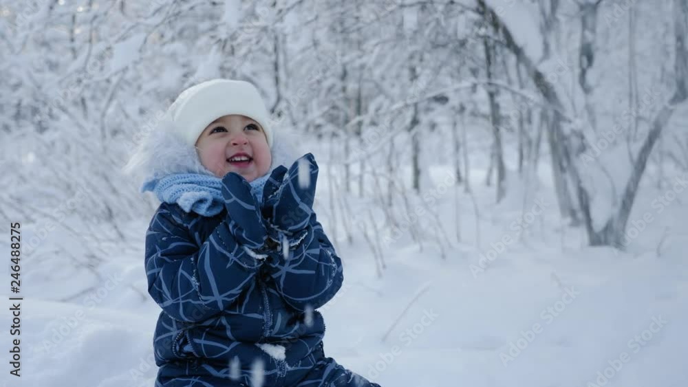 child sitting on the snow in the woods in the winter in a warm blue jumpsuit with fur child sitting on the snow in the woods in the winter in a warm blue jumpsuit with fur