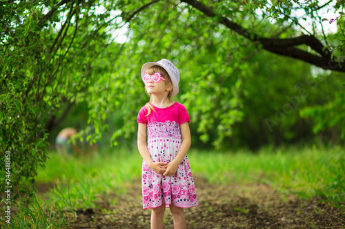 Happy ittle girl in bright dress and funny sunglasses walk in summer garden © Svetlana