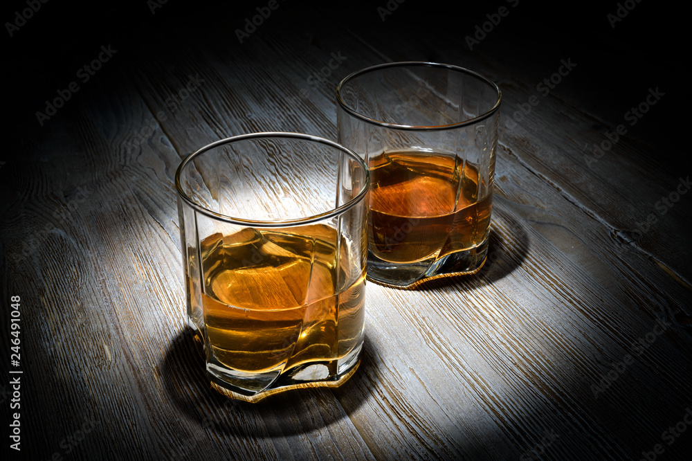 Two glasses of whiskey on a vintage wooden table on a black background.