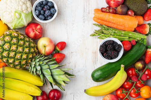 Healthy rainbow fruits vegetables berries, strawberries oranges plums grapes broccoli cauiliflower mango persimmon pineapple on white wooden table, top view, copy space, selective focus