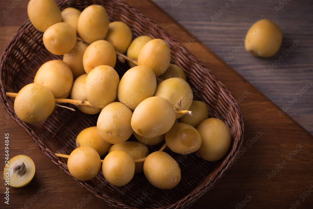 Fresh yellow dates on a sprig in wicker plate on rustic wooden background. Flat lay low key Fresh yellow dates on a sprig in wicker plate on rustic wooden background. Flat lay low key