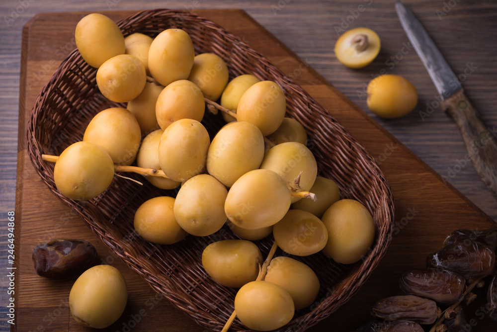 Fresh yellow dates and dried dates on sprigs in wicker plate on rustic wooden background with a knife. Flat lay low key Fresh yellow dates and dried dates on sprigs in wicker plate on rustic wooden background with a knife. Flat lay low key