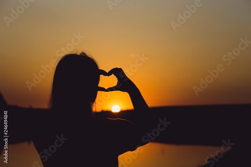 girl shows heart with fingers at sunset close up