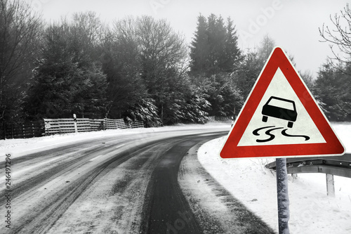 Snowy curvy road with traffic sign. Schleudergefahr auf eisglatter Strasse