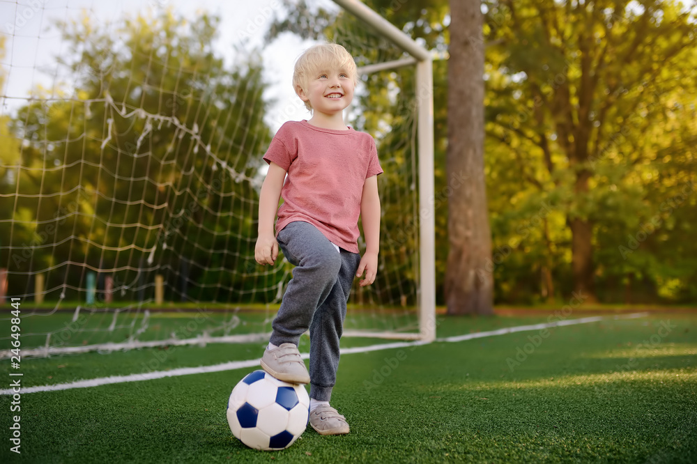 Little boy having fun playing a soccer/football game on summer day. Active outdoors game/sport for children.