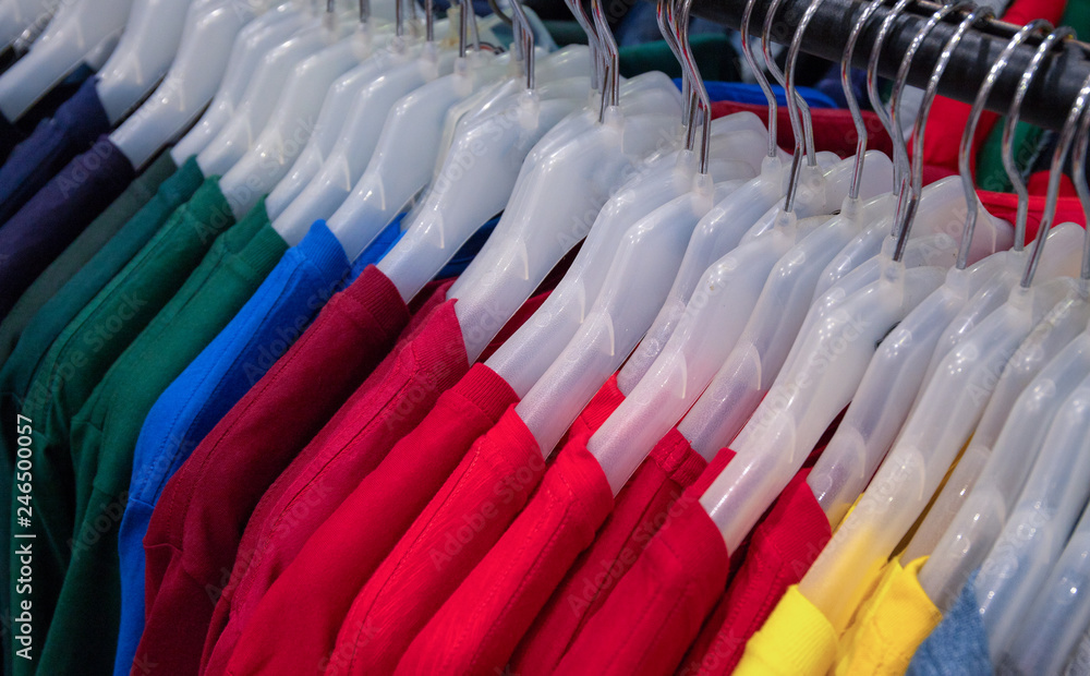 Bright shirts on hangs for sale in shop. Vibrant color polo on wooden hanger. Summer seasonal wear in department store