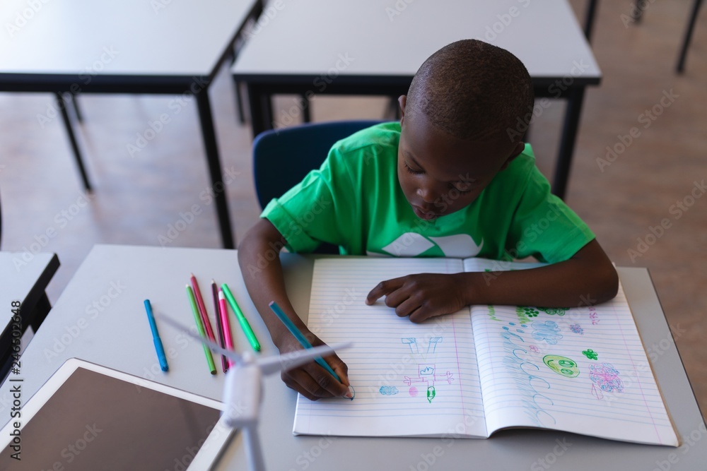 Schoolboy drawing on book at desk in classroom Schoolboy drawing on book at desk in classroom
