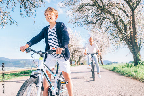 Father and son having fun when riding bicycles on country road under blossom trees. Healthy sporty lifestyle concept image.