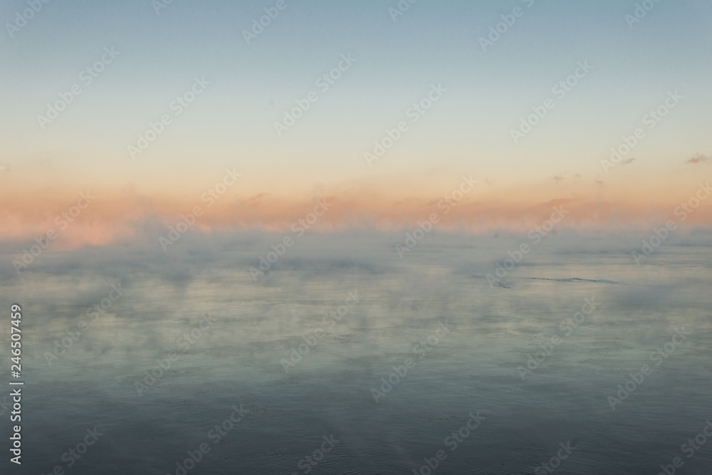 Mist over calm lake in cold of winter with colorful sunset