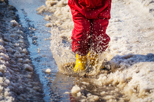 Kid legs in rainboots jumping in the ice puddle photo