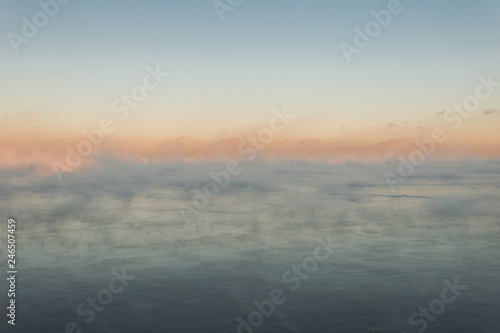 Mist over calm lake in cold of winter with colorful sunset