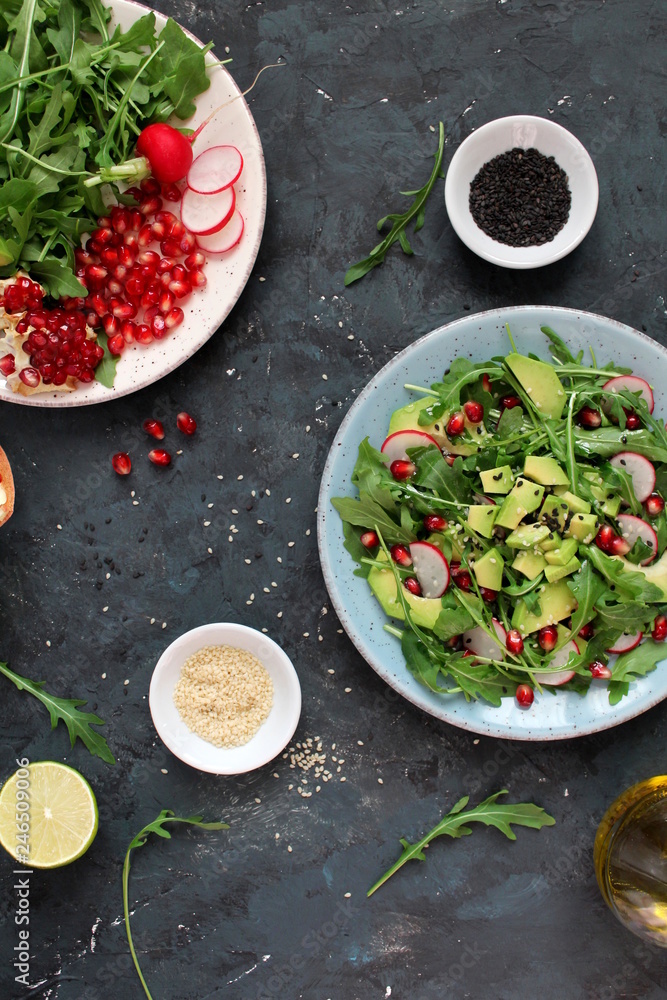 Ingrdient for making salad on dark background. Vegetable salad in plate, avocado, arugula, pomegranate, radish and sesame. Top view with copy space. Vegetarian and vegan food. Ingrdient for making salad on dark background. Vegetable salad in plate, avocado, arugula, pomegranate, radish and sesame. Top view with copy space. Vegetarian and vegan food.