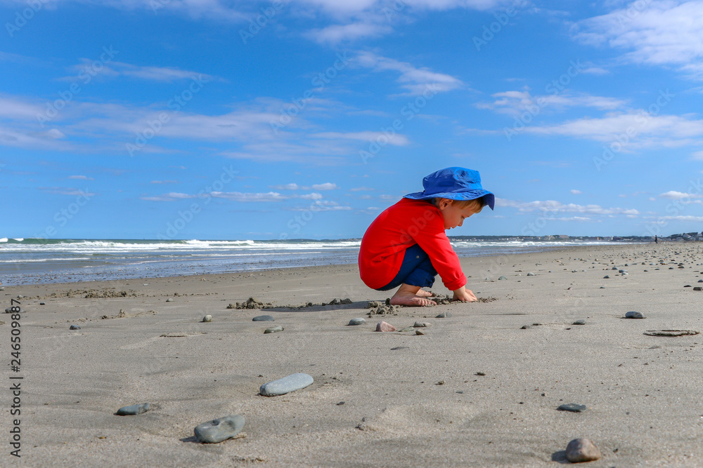 toddler boy wearing blue hat plays in sand at the beach toddler boy wearing blue hat plays in sand at the beach