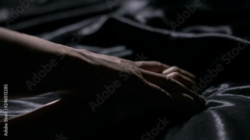 Hot couple holding hands sensually on black silk bed.