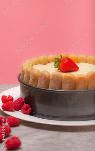 Diplomat cake or Charlotte Cake with strwaberries and lady fingers in baking pan on a wooden table with pink background / Focus on top strawberry photo