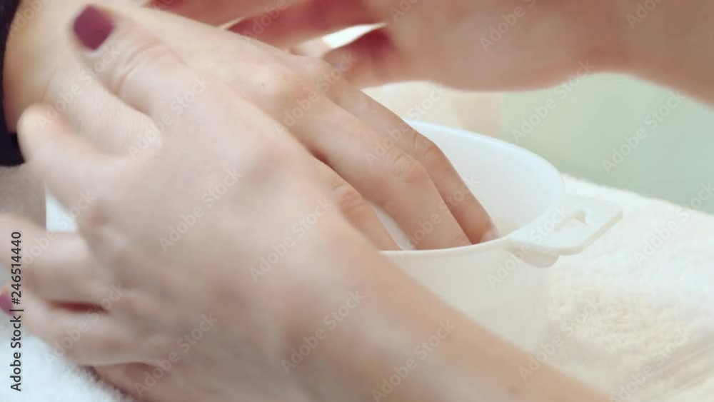 girl douses her fingernails in a hand soak bowl for making manicure in a beauty salon, manicurist takes a white hand soak bowl from the table then puts girl's hand on it and douses girls fingers girl douses her fingernails in a hand soak bowl for making manicure in a beauty salon, manicurist takes a white hand soak bowl from the table then puts girl's hand on it and douses girls fingers
