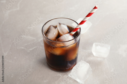 Glass of refreshing cola with ice on grey background
