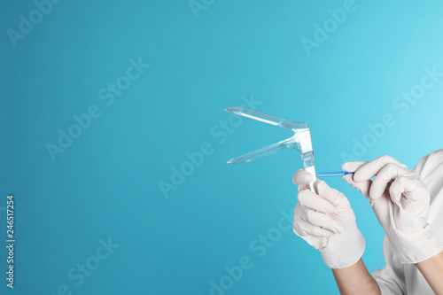 Female doctor holding vaginal speculum on color background, closeup view with space for text. Medical object photo
