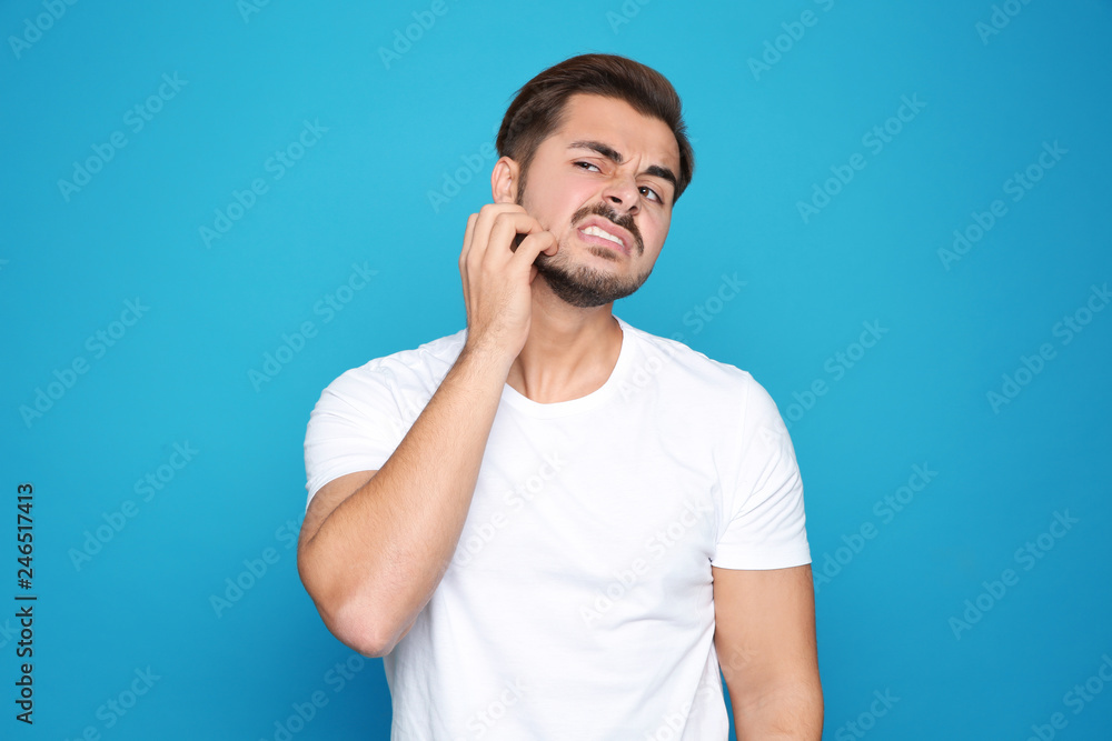 Young man scratching face on color background. Annoying itch Young man scratching face on color background. Annoying itch