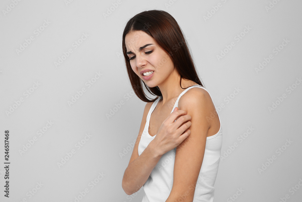 Young woman scratching shoulder on light background. Annoying itch Young woman scratching shoulder on light background. Annoying itch