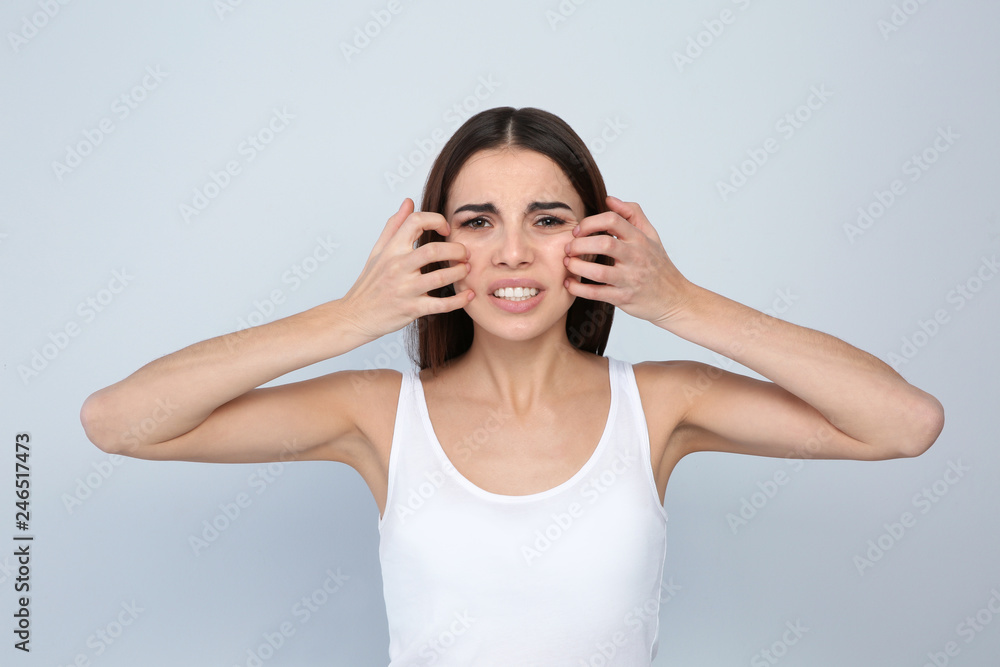 Young woman scratching face on light background. Annoying itch - obrazy, fototapety, plakaty 