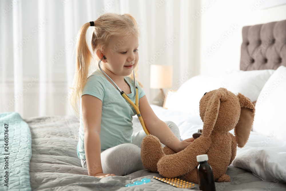 Cute child imagining herself as doctor while playing with stethoscope and toy bunny at home Cute child imagining herself as doctor while playing with stethoscope and toy bunny at home