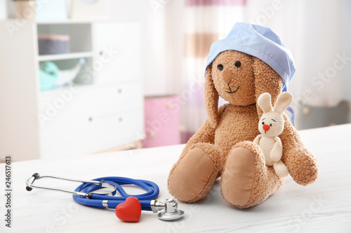 Composition with toy bunnies, stethoscope and heart on table indoors, space for text. Children's doctor