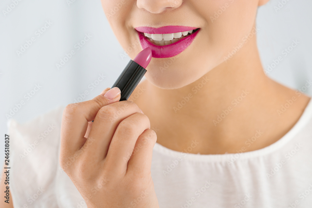 Beautiful woman applying lipstick on light background, closeup Beautiful woman applying lipstick on light background, closeup