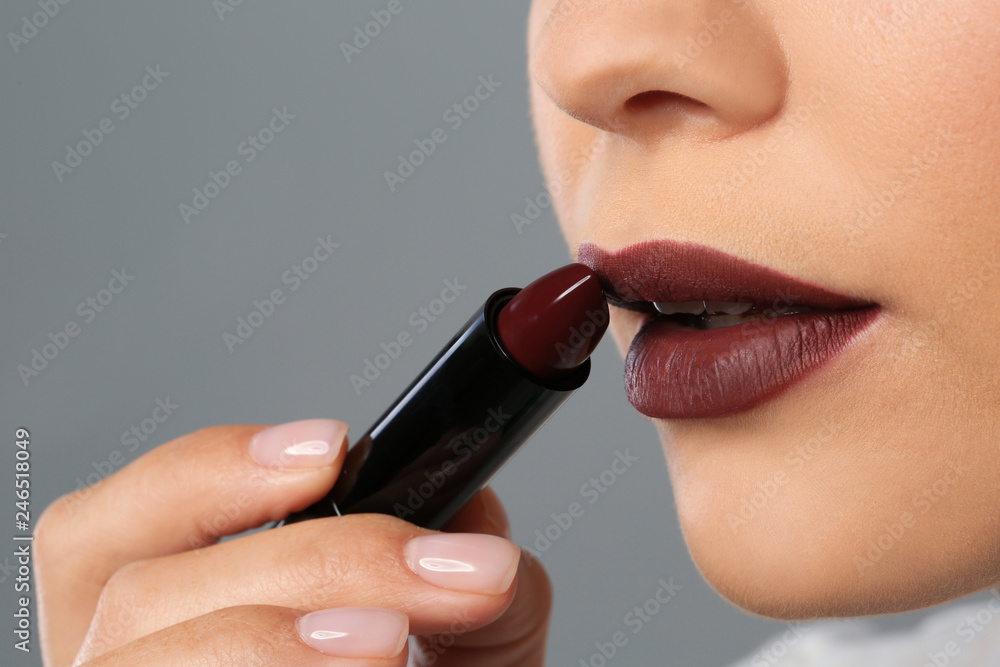 Naklejka premium Beautiful woman applying dark lipstick on gray background, closeup