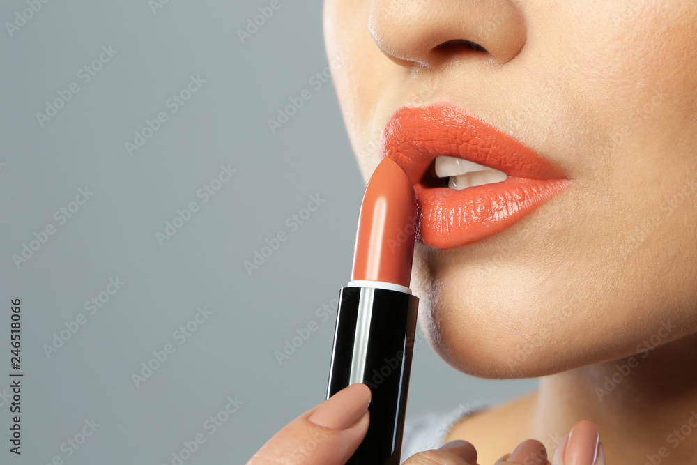 Obraz premium Young woman applying beautiful lipstick on gray background, closeup. Space for text