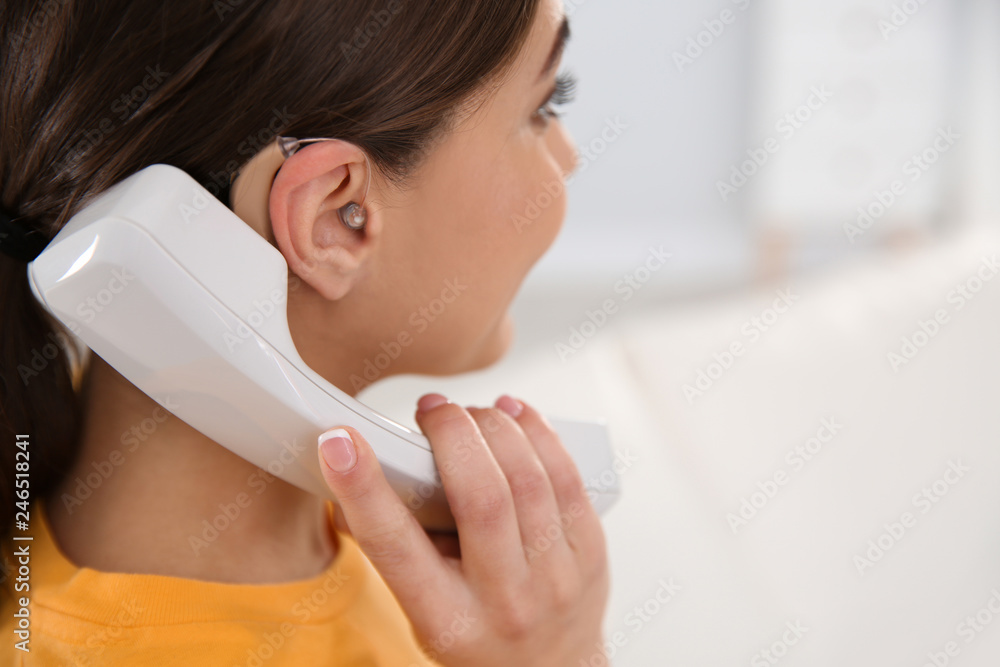 Young woman with hearing aid talking on phone indoors, closeup. Space for text Young woman with hearing aid talking on phone indoors, closeup. Space for text