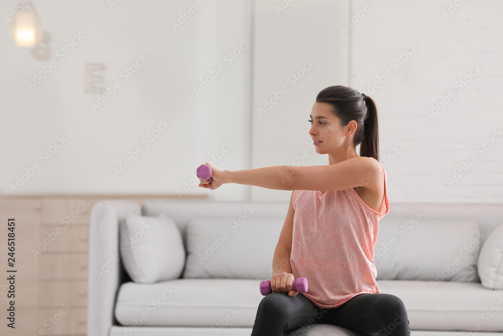 Young woman in fitness clothes doing exercise with dumbbells at home. Space for text Young woman in fitness clothes doing exercise with dumbbells at home. Space for text