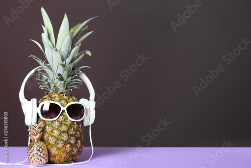 Pineapple with headphones and sunglasses on table against dark background. Space for text