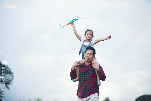 Asian child girl and father with a kite running and happy on meadow in summer in nature