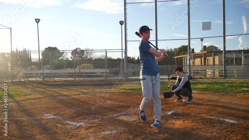 A young man baseball player swings his bat at the ball and misses the pitch during a team practice in the park at sunset.