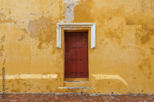 Close up of old wood red door weathered yellow walls on a church in Latin America