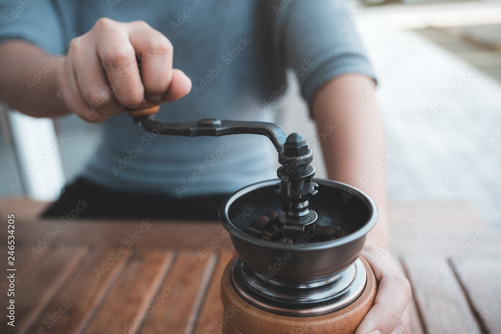 Closeup image of a woman's hands using vintage wooden coffee grinder to mill coffee beans Closeup image of a woman's hands using vintage wooden coffee grinder to mill coffee beans