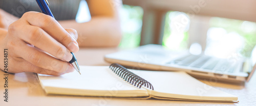 Woman hand is writing on notepad with pen in office.