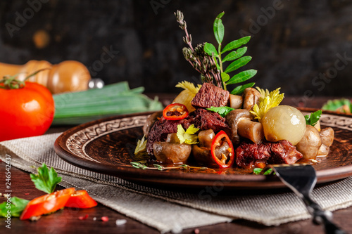 Fototapeta Naklejka Na Ścianę i Meble -  French cuisine concept. blanquette of veal with mushrooms, whole stewed onions, carrots and chilli peppers. Serving dishes in the restaurant in a ceramic plate, next to vegetables.