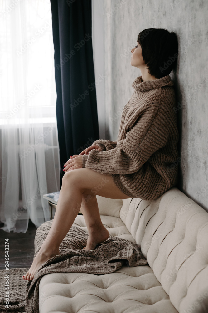 Gorgeous young brunette woman in warm knitted sweater posing on the bed in cozy appartments Gorgeous young brunette woman in warm knitted sweater posing on the bed in cozy appartments