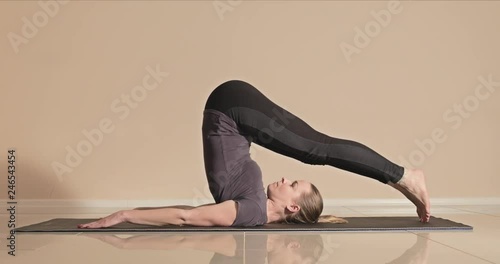 Young female yoga instructor demonstrates the plow pose also known as Halasana, profile side view in a yoga studio, feet to the left photo