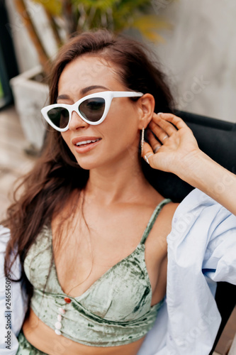 Beautiful stylish elegant woman in fashionable glasses and velvet swimsuit and  blue shirt relaxing on modern spa resort with happy smile in good sunny day