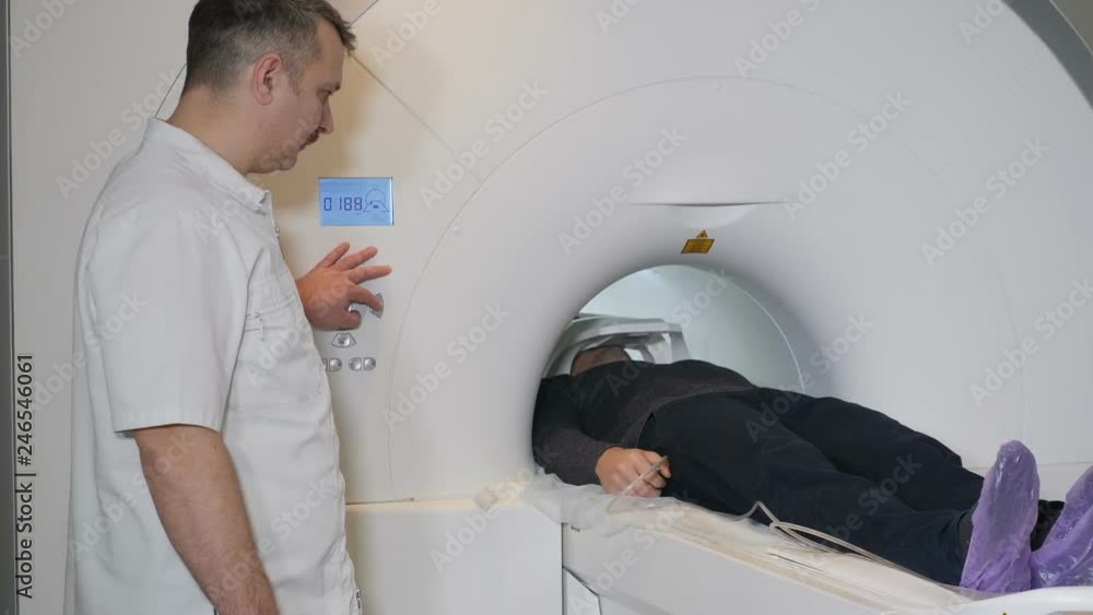 Male patient is moving into a CT-scanner. Medical equipment: computed tomography machine in diagnostic clinic. Health concept. Doctor presses settings button of CT MRI scanner. hd Male patient is moving into a CT-scanner. Medical equipment: computed tomography machine in diagnostic clinic. Health concept. Doctor presses settings button of CT MRI scanner. hd
