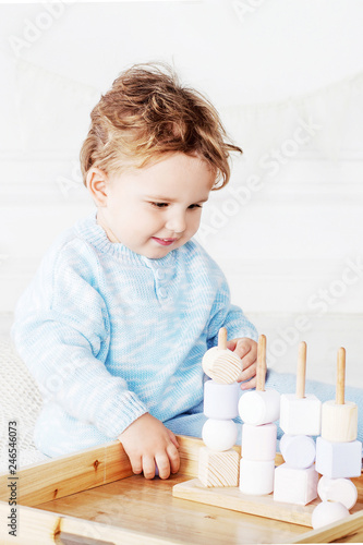 Child boy playing in his room with a wooden toy sorter. Smiling cute boy with natural toys.