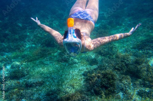 Young woman diving undersea. Snorkel in coral reef of tropical sea. Woman in full-face snorkeling mask.