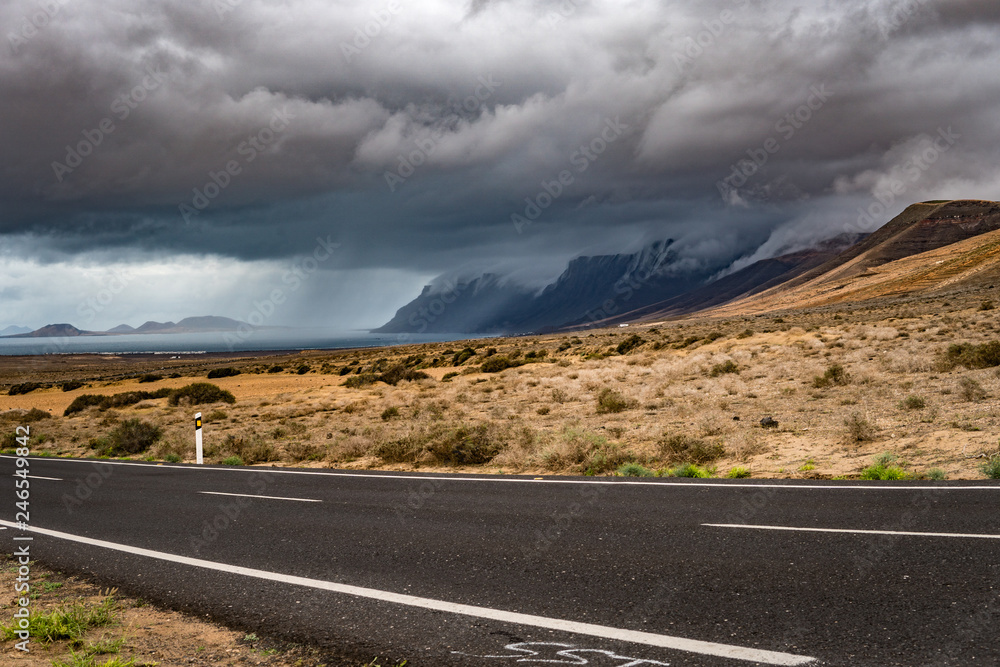 Fototapeta premium Huge and beautiful storm over Playa Famara beach and in Lanzarote, and La Graciosa Island. Beautiful thunderstorm in Canary Islands. Rain in the background