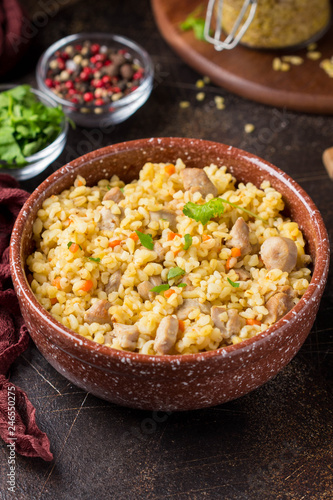 Bulgur with turkey, pork or beef. Eastern dish of rice, tasty traditional food. Stewed meat with grits. Pilaf on dark background