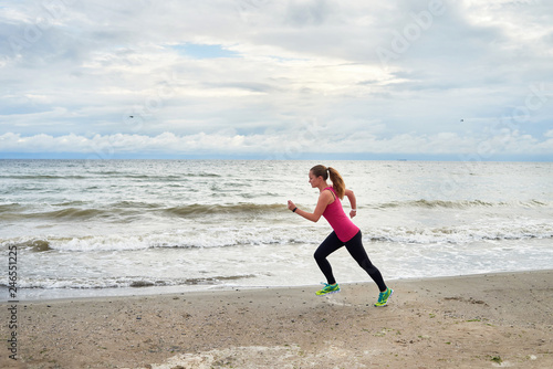 Athletic woman running on sea beach, copy space. Female runner working out at summer morning, full length body portrait, side view. Healthy lifestyle concept