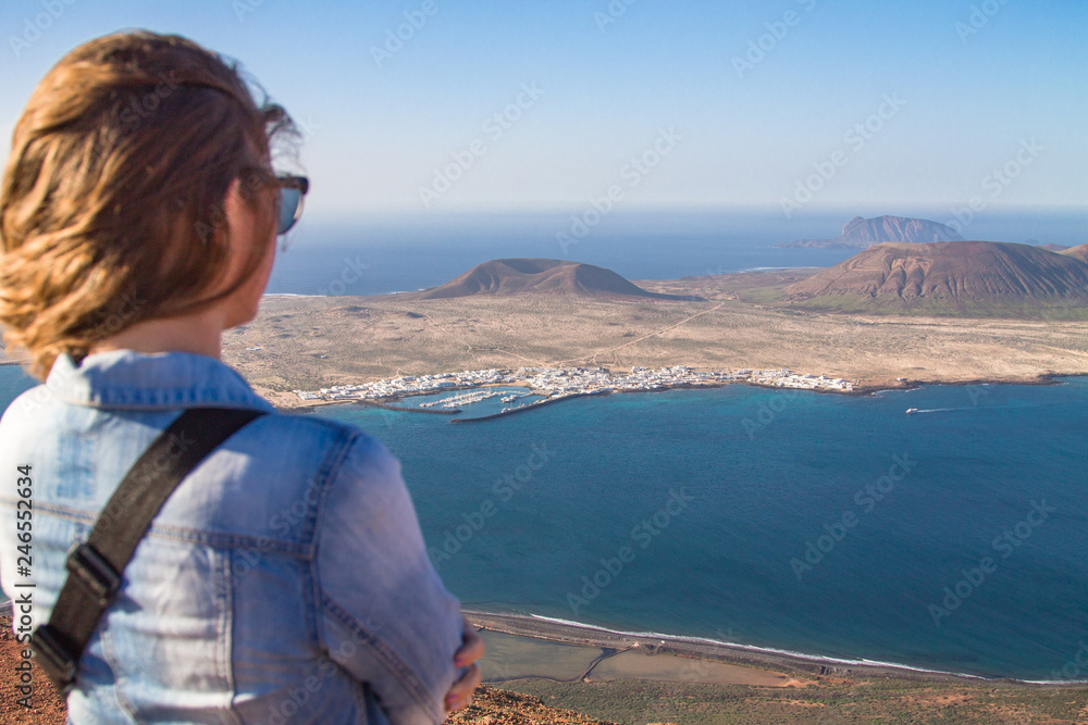 A girl stands turned backs against the background of the Atlantic Ocean and the island of La Graciosa. Mountain. Mirador del Rio. North of Lanzarote. Canary Islands. Spain A girl stands turned backs against the background of the Atlantic Ocean and the island of La Graciosa. Mountain. Mirador del Rio. North of Lanzarote. Canary Islands. Spain