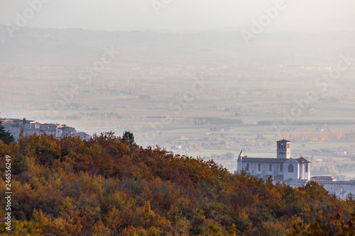 Beautiful view of Assisi town (Umbria) and St.Francis church in autumn from an unusual place, behind an hill with orange and yellow trees